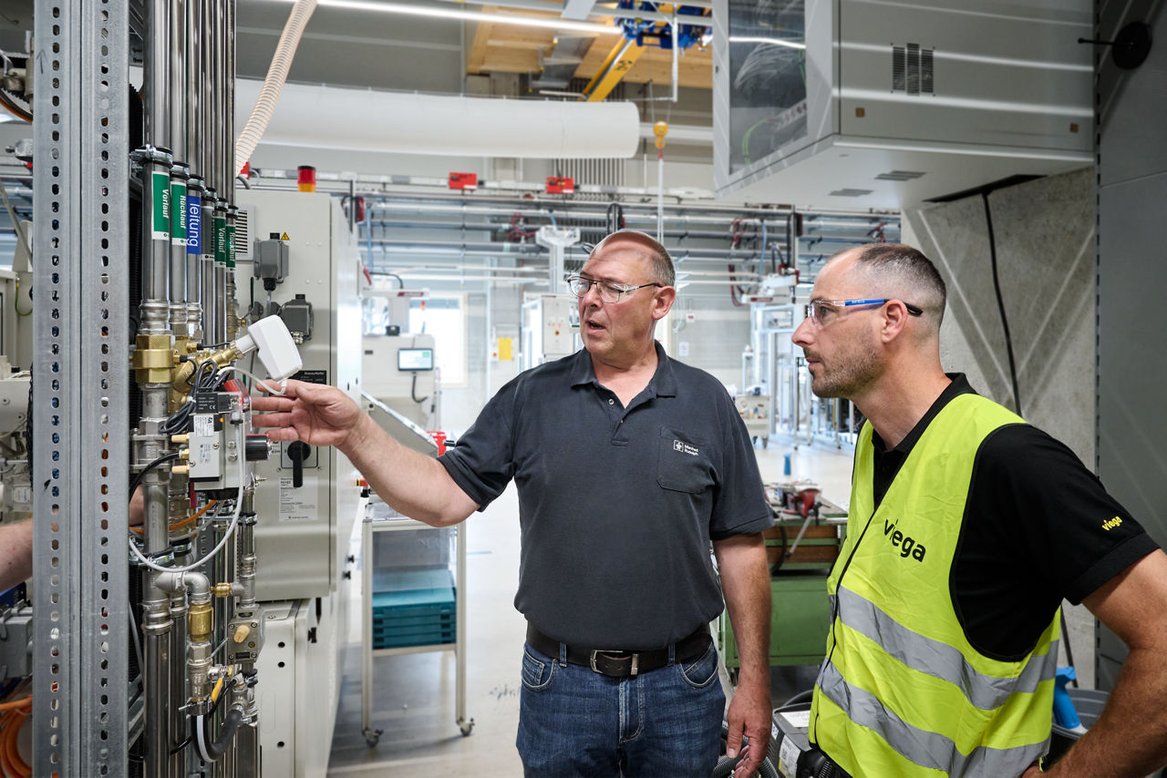 Manfred Rudolph (links) vom Instandhaltungsteam des Kunststoffverarbeiters Pöppelmann und ein Viega Mitarbeiter schauen auf die Anlagen von Pöppelmann.