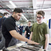 Auszubildender Berat Alp erklärt Luca Dittmann (r.) anhand eines Werkzeugs, was seine Tätigkeit als angehender Zerspanungsmechaniker umfasst. (Foto: Viega)